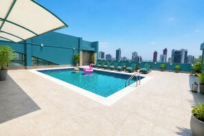 Una piscina en la azotea con vistas al horizonte urbano, sillas de descanso y plantas en macetas.