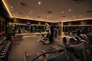Een sportschool met diverse trainingsapparaten, spiegels en een televisiescherm.