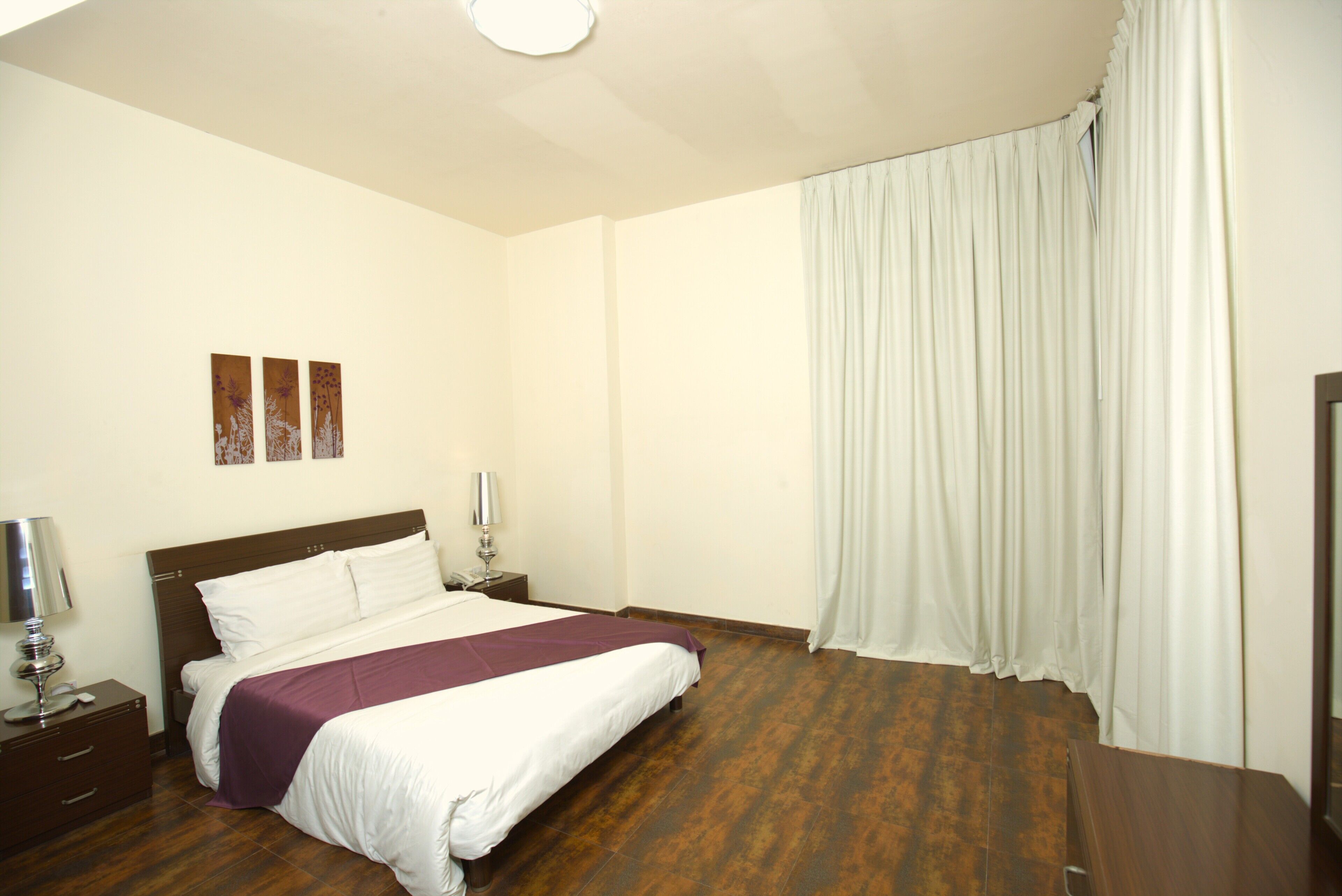 Quarto de hotel com uma cama, mesas de cabeceira, abajur e janela com cortinas.