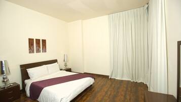 Quarto de hotel com uma cama, mesas de cabeceira, abajur e janela com cortinas.