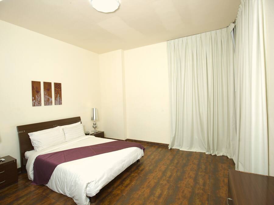 Quarto de hotel com uma cama, mesas de cabeceira, abajur e janela com cortinas.