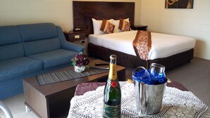 Habitación de hotel con cama, sofá azul, mesita de noche, mesa con una botella de champán y una copa, y dos lámparas fijadas a la pared.