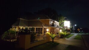 Una casa de dos pisos con un balcón, un coche estacionado en frente y una entrada bien iluminada.