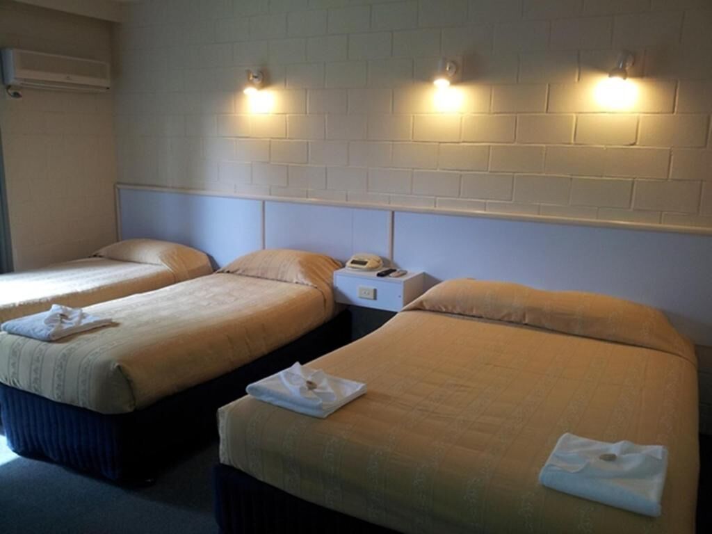 Two single beds with headboards, a nightstand with a phone and a box, and a wall-mounted light fixture.