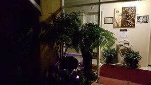 Un área de recepción con puerta de vidrio, plantas en macetas, una escultura y un letrero que indica una zona de silencio.