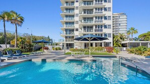 Un hôtel moderne doté d’une grande piscine, d’un espace extérieur aménagé et de palmiers.