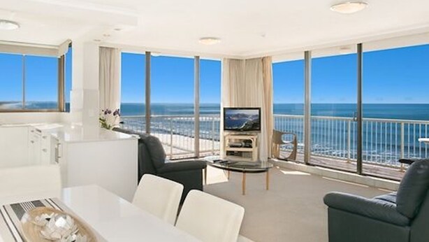Un salon moderne doté d’un grand téléviseur, de sièges confortables et d’un balcon offrant une vue sur la mer.