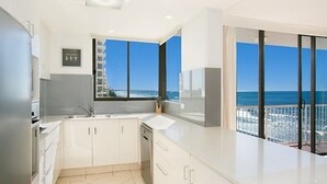 Une cuisine moderne dotée d’une grande fenêtre, d’un balcon avec vue sur la mer et d’un plafond haut.