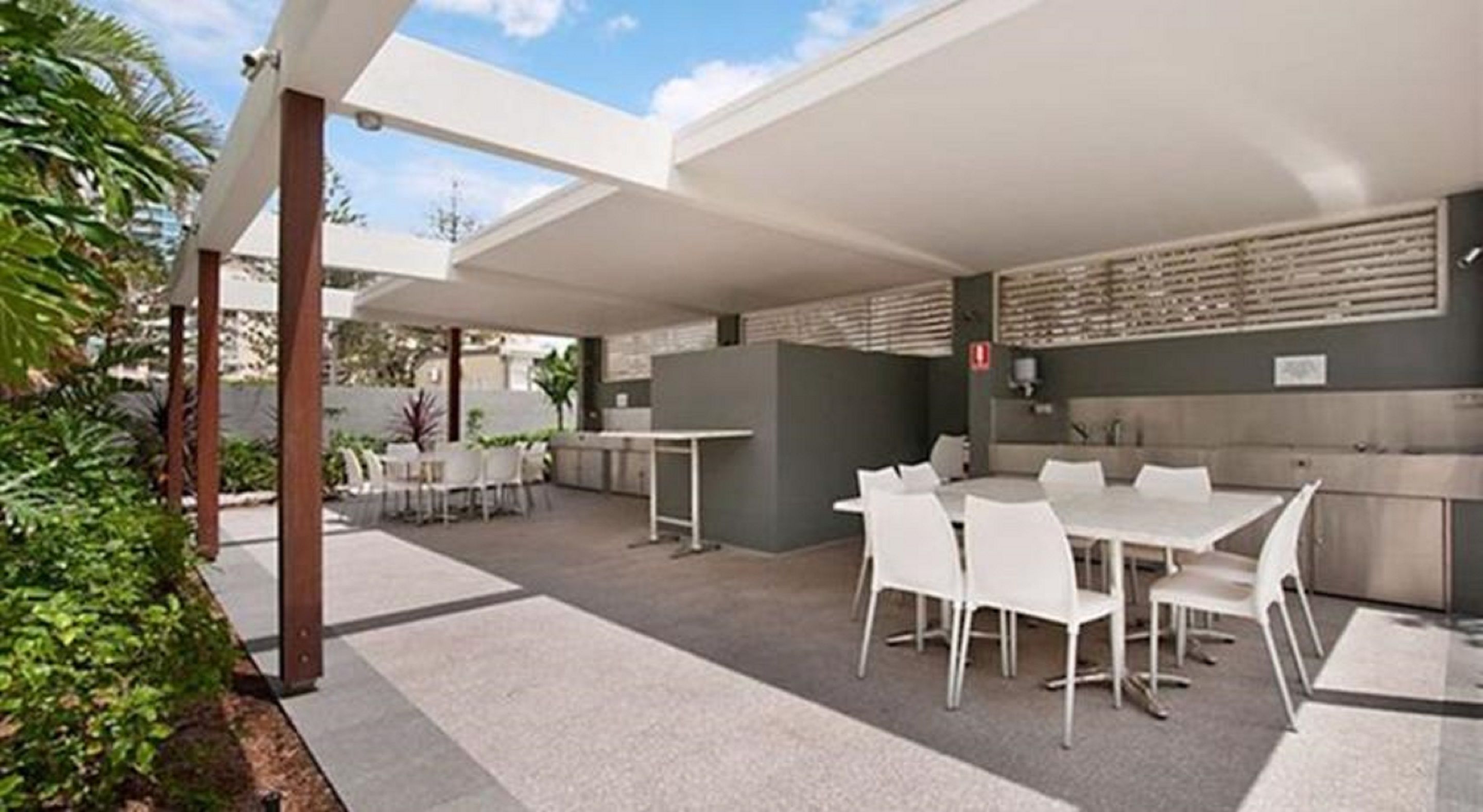 Un'area patio esterna con tavoli e sedie bianche, una zona cucina e vista sul cielo.