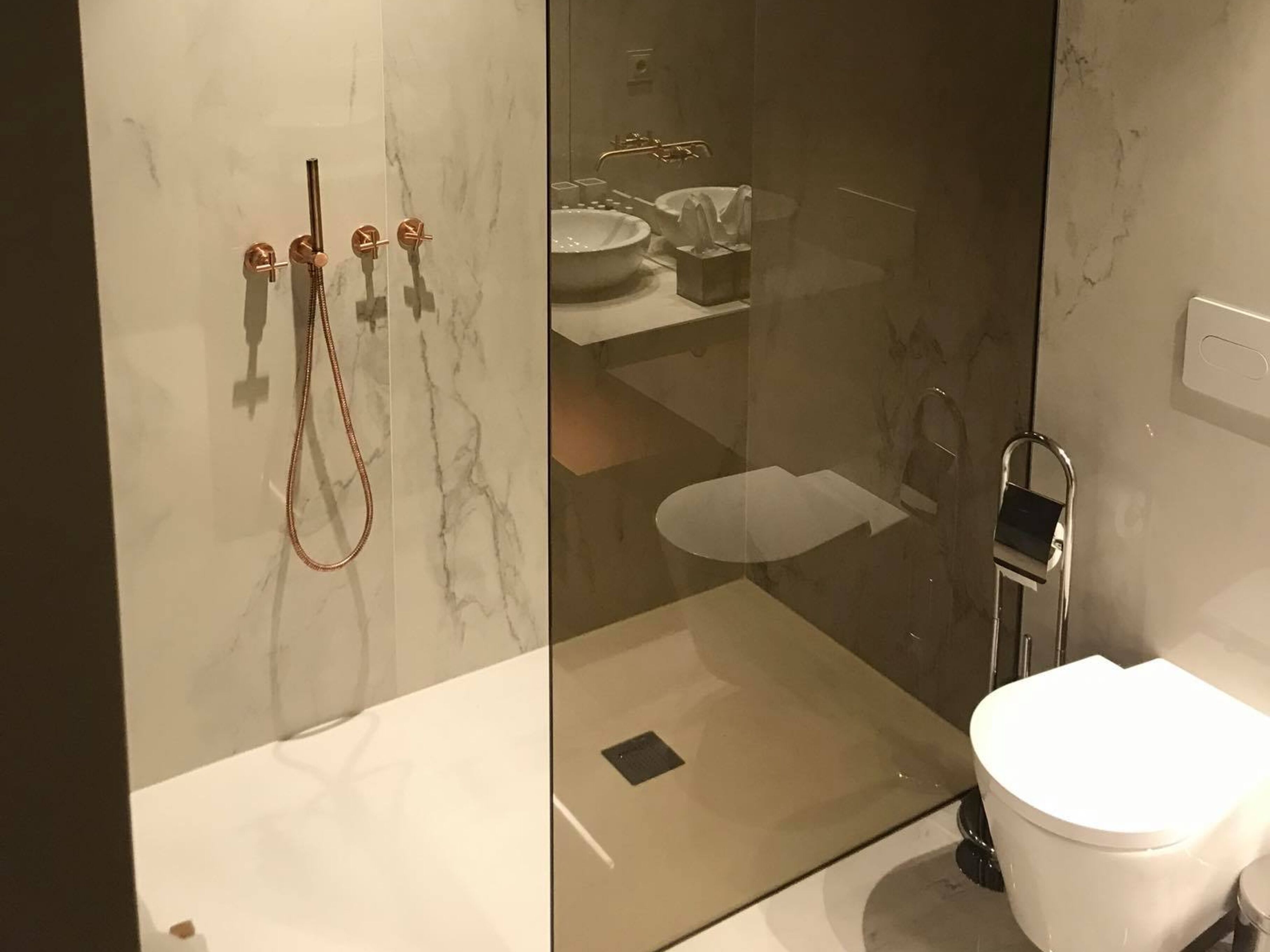Un baño moderno con ducha envuelta en vidrio, inodoro blanco y lavamanos con encimera de mármol.