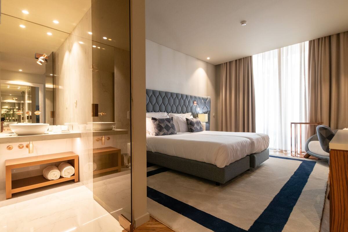 Ein modernes Hotelzimmer mit einem großen Bett, einem Badezimmer mit großem Spiegel und Blick ins Freie.
