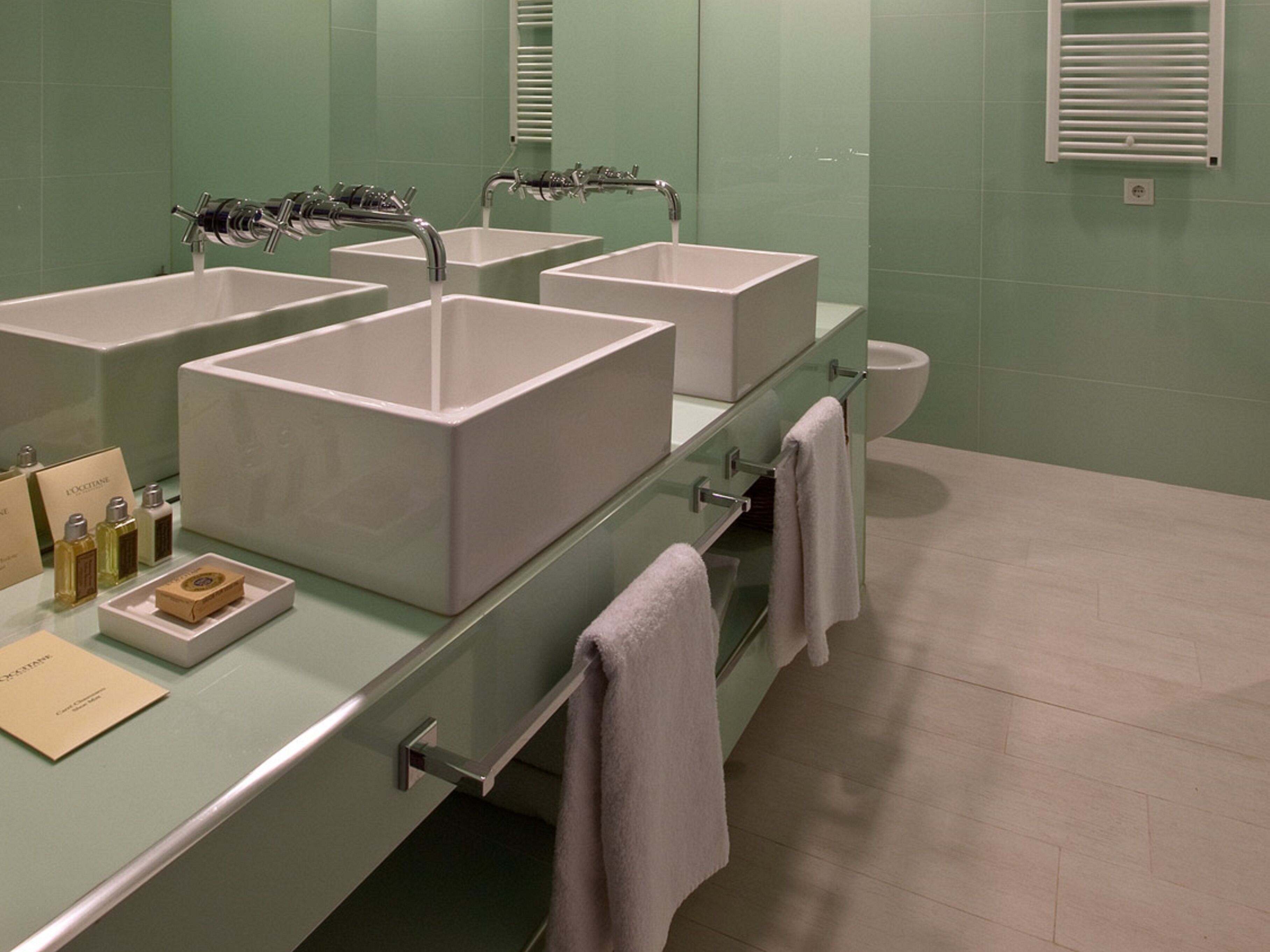 Un baño moderno con cuatro lavamanos blancos, un tocador de vidrio y un inodoro.