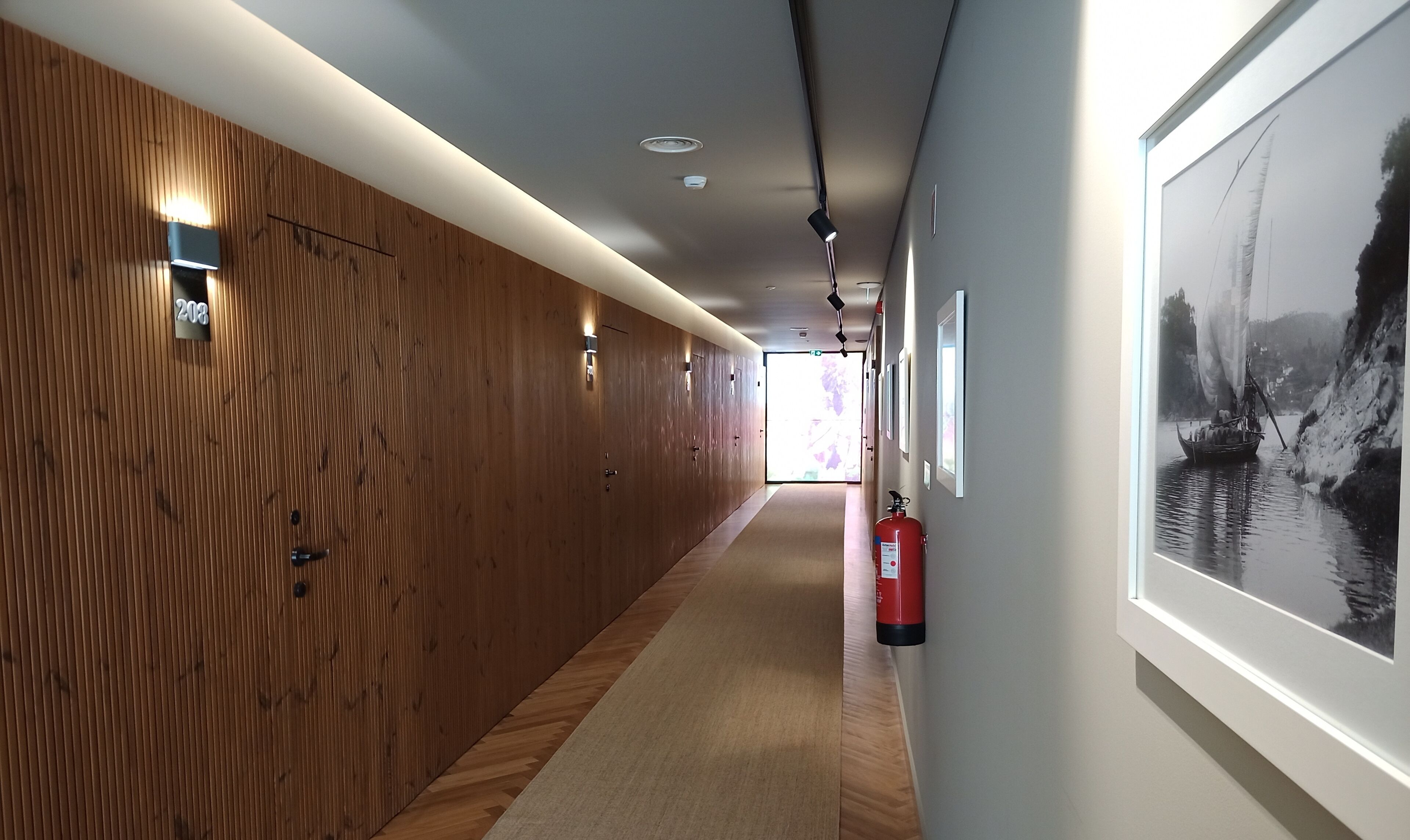A hallway with wooden paneling, a fire extinguisher, and framed artwork on the walls.
