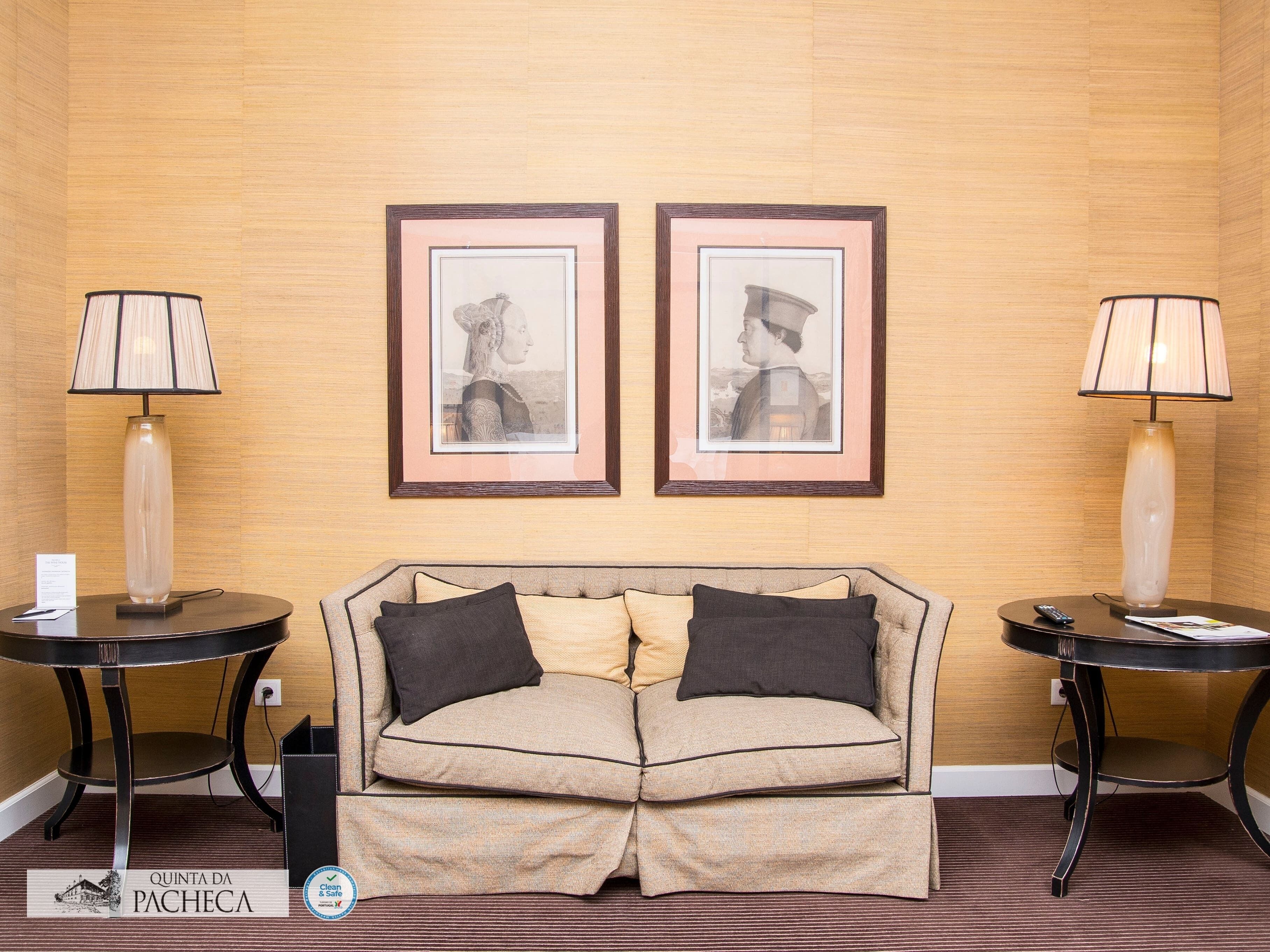 A hotel room with a sofa, two framed pictures on the wall, and two lamps on side tables.