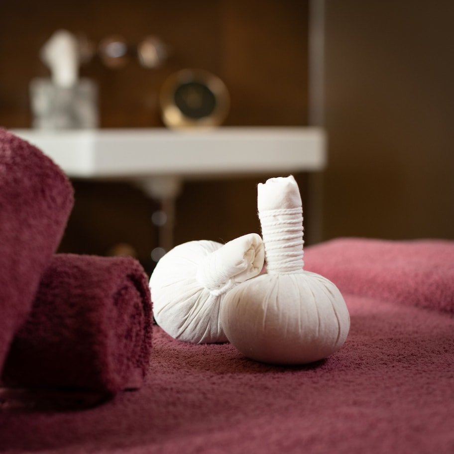 A spa setting with a rolled-up towel and a white massage tool on a purple towel.