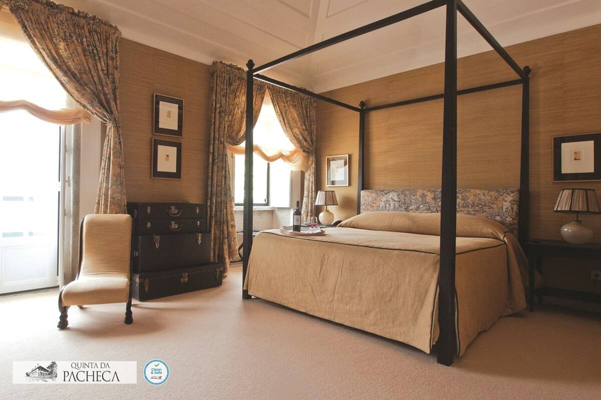 Ein Raum mit einem Himmelbett, einem klassischen Design, einer Holzkommode und einem Sessel.