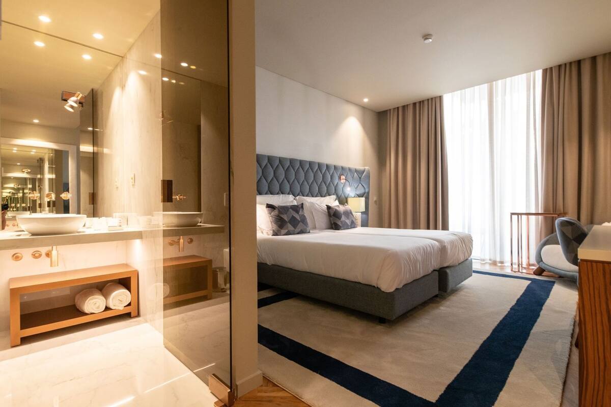 Ein modernes Hotelzimmer mit einem großen Bett, einem Badezimmer mit Waschtisch und Blick ins Freie.