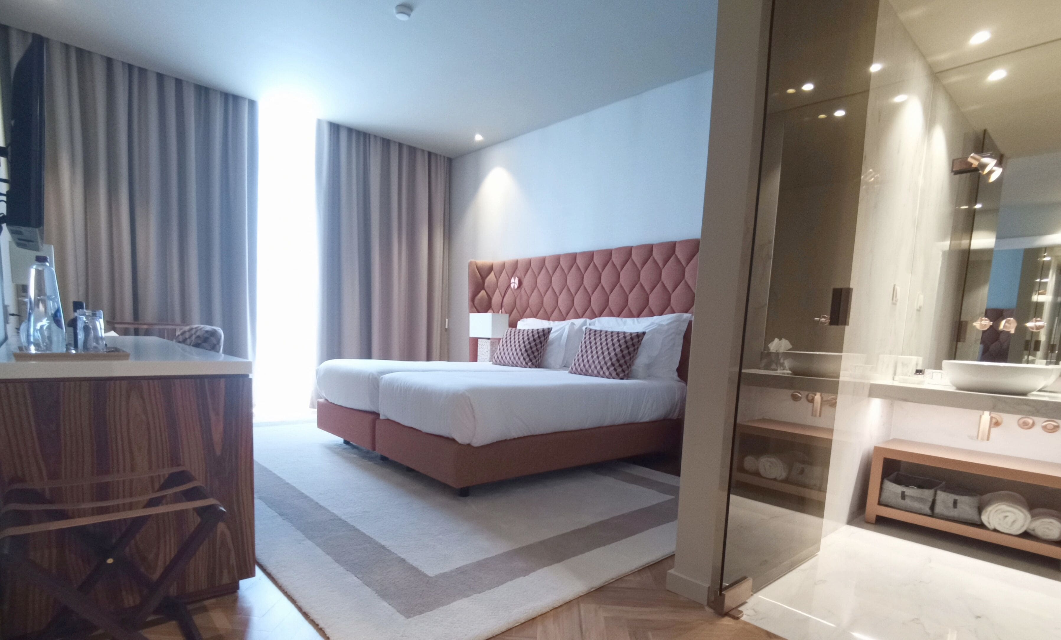 Une chambre d’hôtel moderne dotée d’un grand lit, d’un bureau avec une chaise, d’une douche en verre et d’une coiffeuse avec un miroir.
