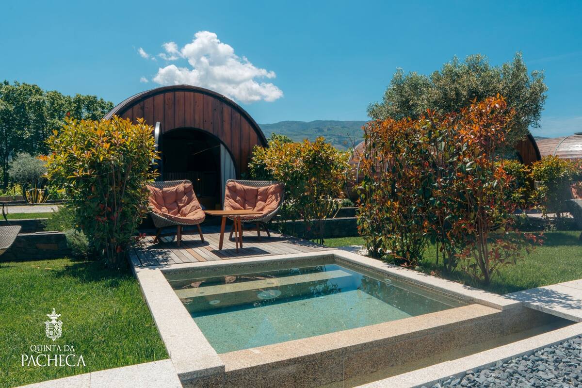 Ein Poolbereich mit zwei Korbstühlen, einer Holzkonstruktion und Blick auf Hügel.