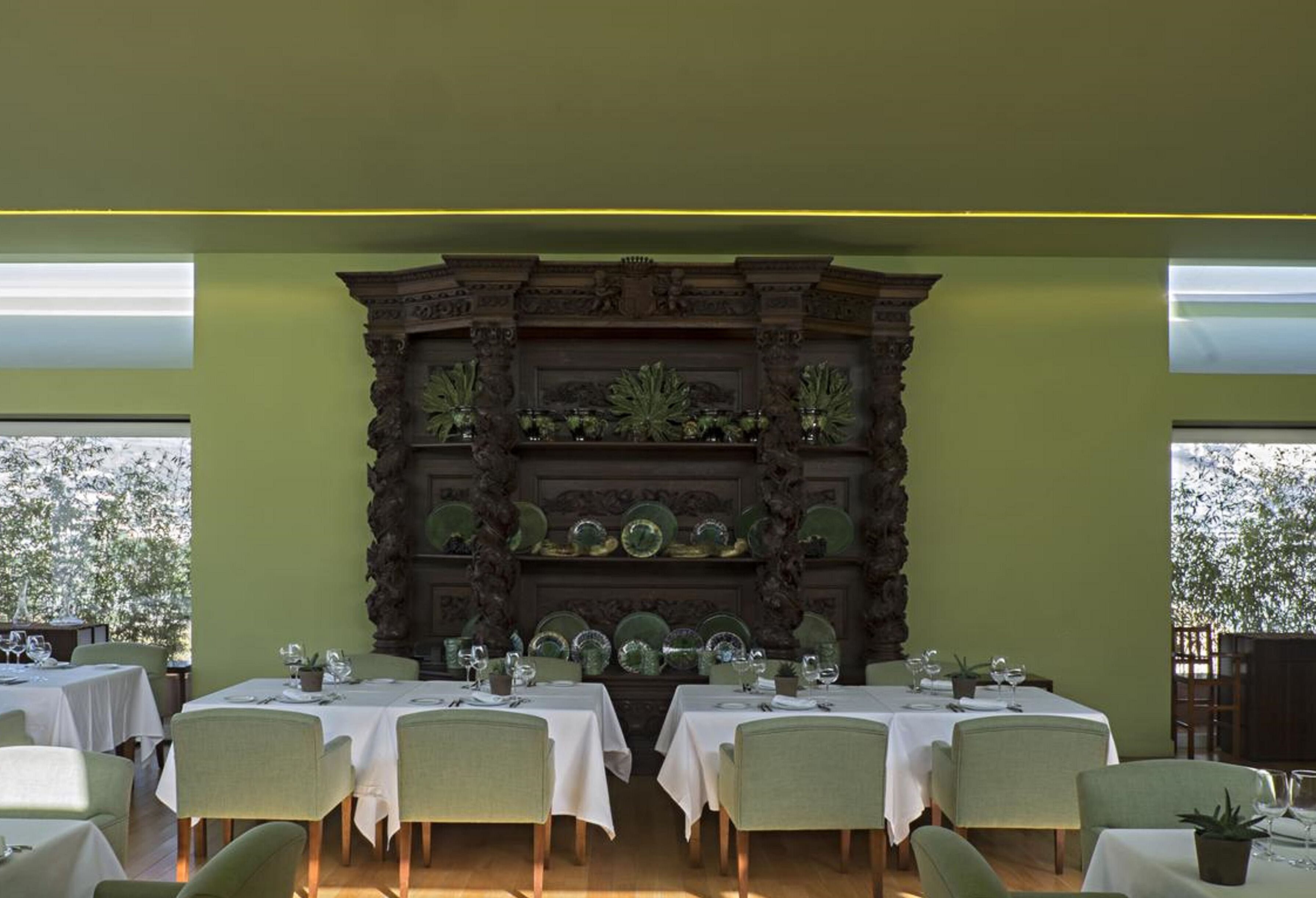 Un espace repas avec des tables dressées, un mur décoratif orné de motifs végétaux et de grandes fenêtres laissant entrer la lumière naturelle.