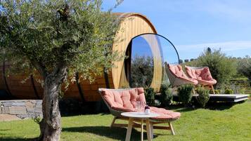 Une structure en bois dotée d’une grande fenêtre circulaire, de deux fauteuils roses rembourrés et d’une table sur laquelle se trouvent une bouteille et un verre.