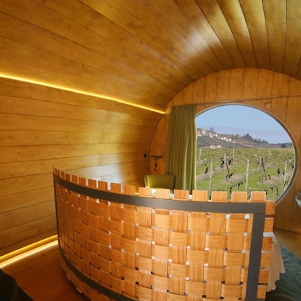 A wooden interior with a curved wooden partition, a round window, and a view of vineyards.