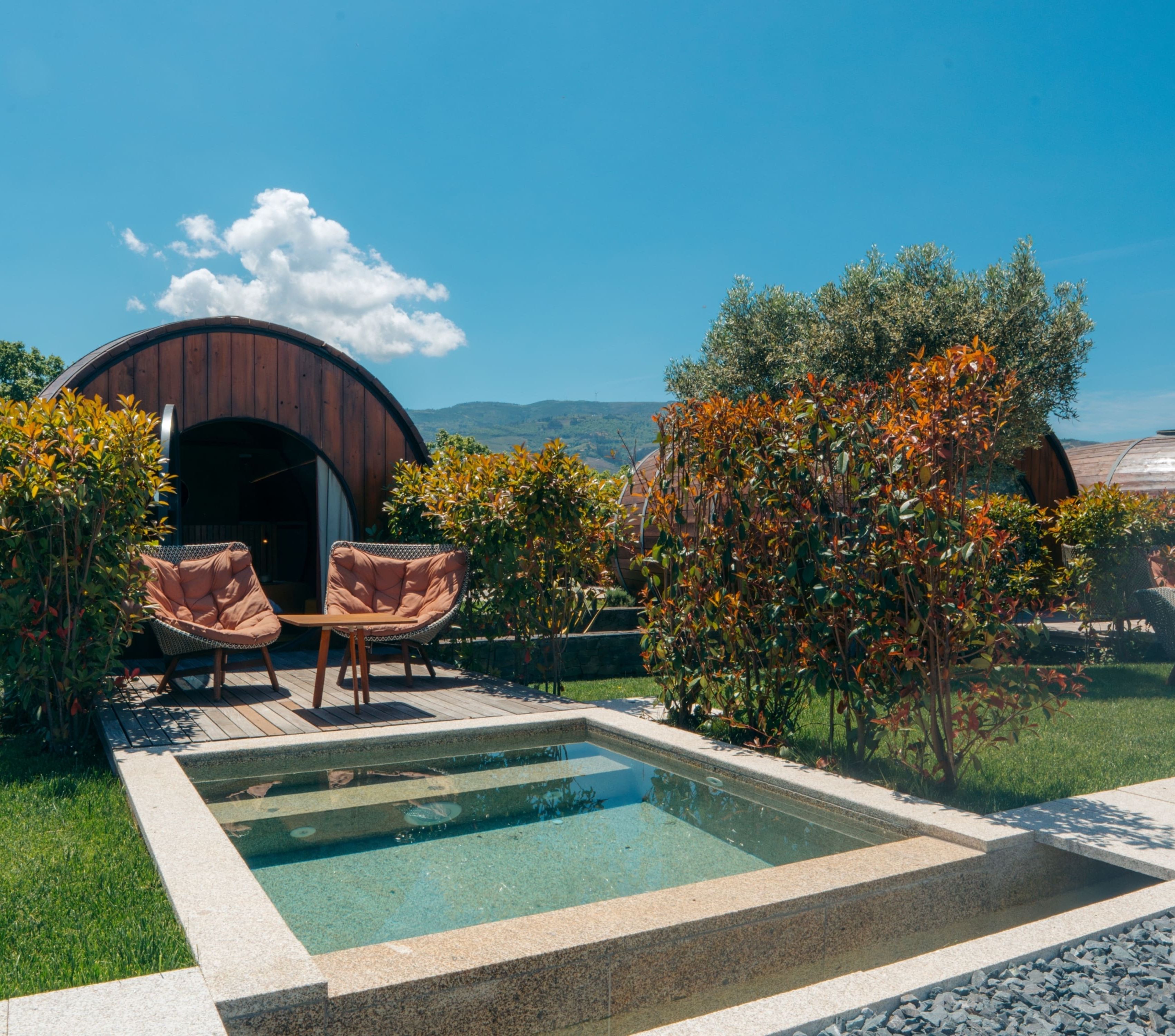 Zona de piscina con dos sillas de mimbre, una estructura de madera y vistas a colinas.