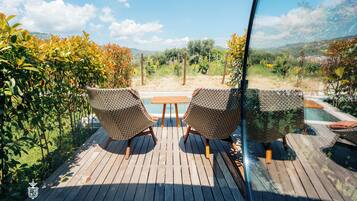 A wooden deck with two wicker chairs and a small table, overlooking a pool and lush greenery.