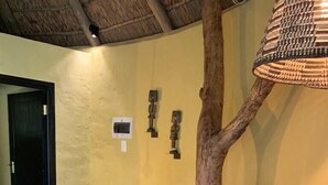 Une pièce avec un plafond en chaume, une chaise en osier, une table en bois et un tapis en peau de vache.
