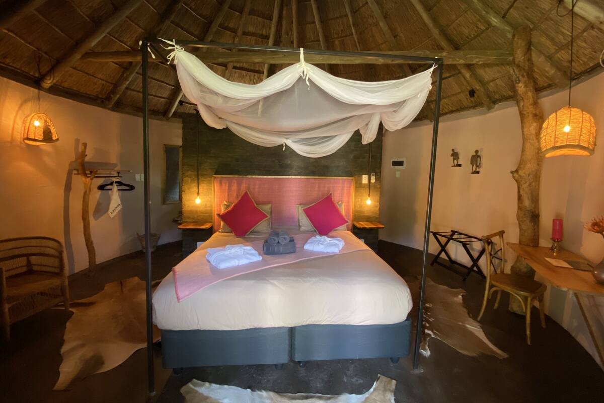 A room with a bed under a canopy, a wooden ceiling, and a small table with a chair.