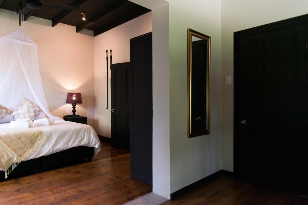 A bedroom with a canopy bed, a bedside table with a lamp, and a large mirror on the wall.