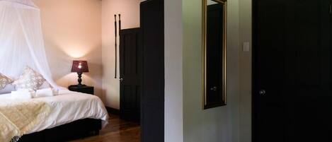A bedroom with a canopy bed, a bedside table with a lamp, and a large mirror on the wall.