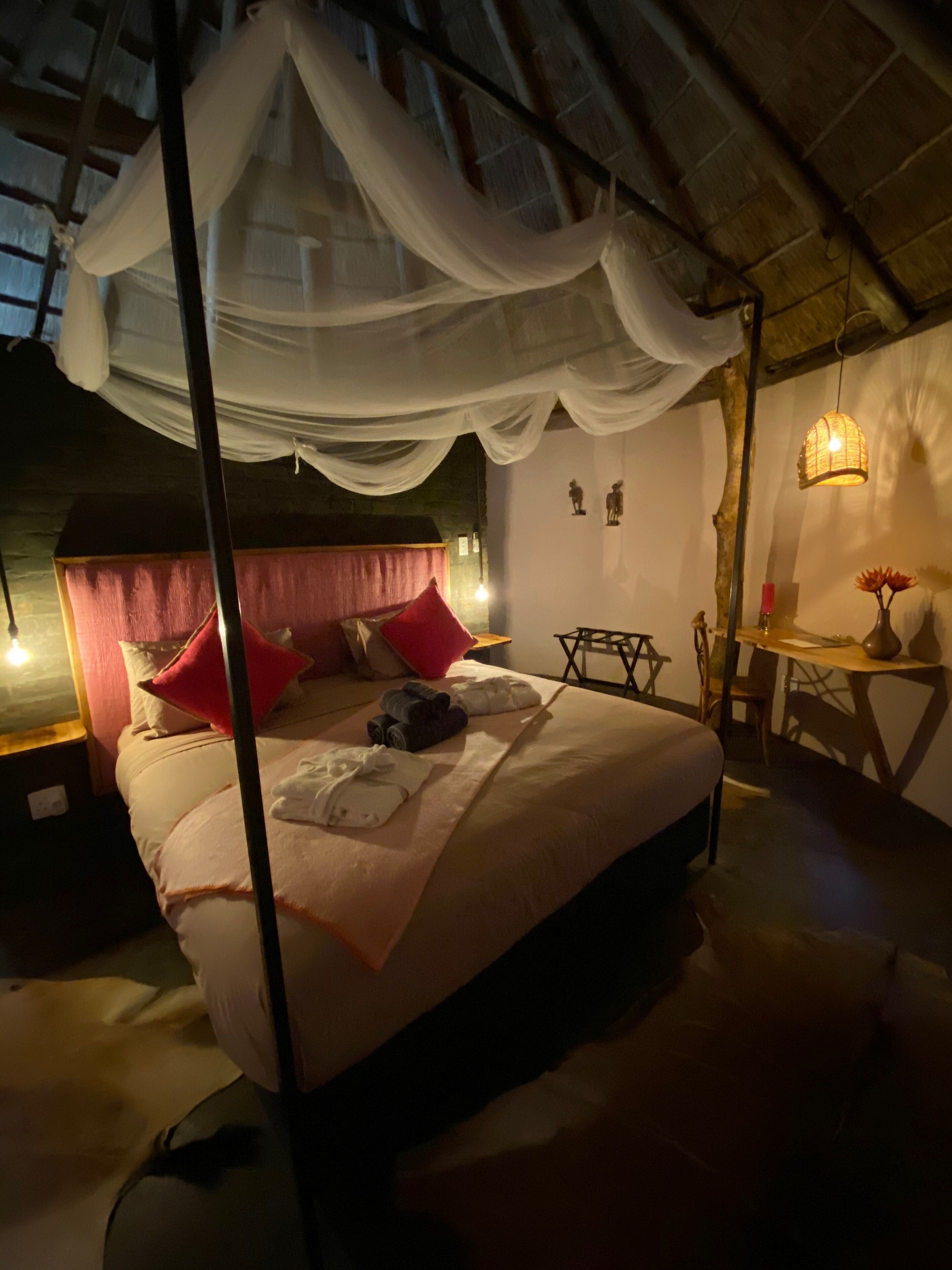 Un dormitorio con cama con dosel, una mesita con un florero y una silla.