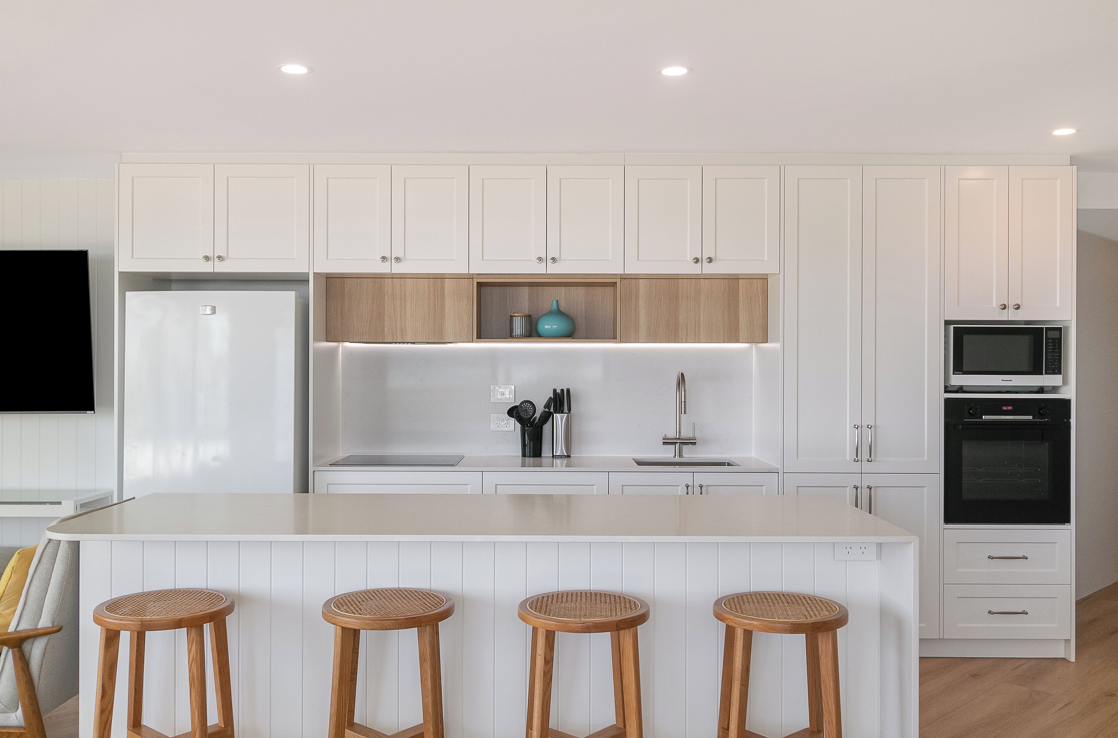 Una cucina moderna con mobili bianchi, un'isola centrale con sgabelli, un forno integrato e un microonde.