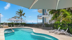 A swimming pool with lounge chairs, a covered area, and a view of the ocean. - Oceanside Resort (Bilinga)