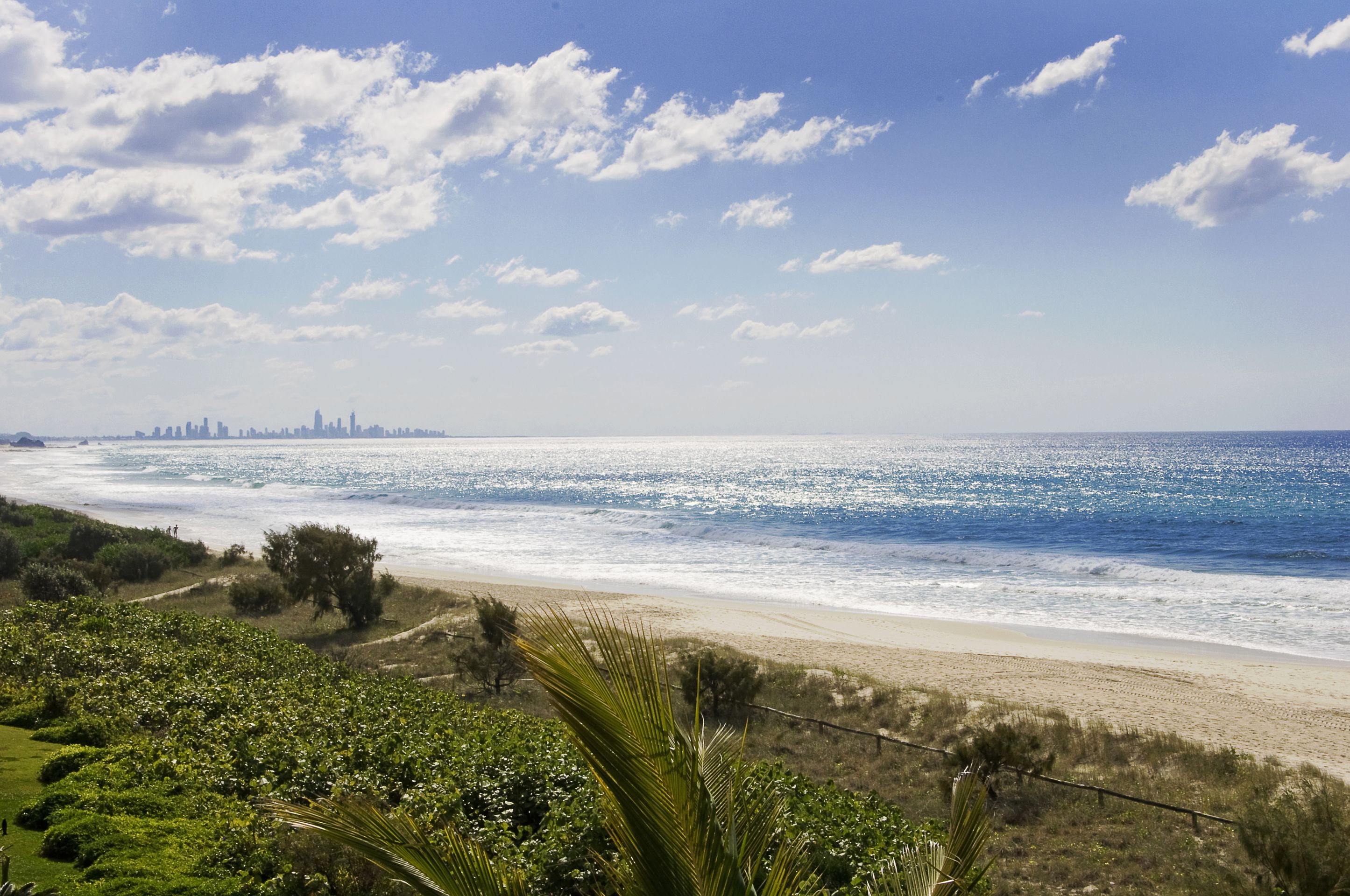 Eine Küstenlandschaft mit Strand, Meer und weiter Stadtansicht am Horizont.