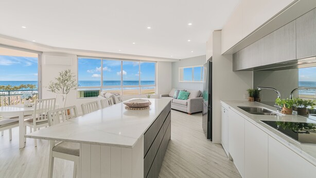 A modern kitchen with a large island, white cabinetry, and a view of the ocean. - Oceanside Resort (Bilinga)