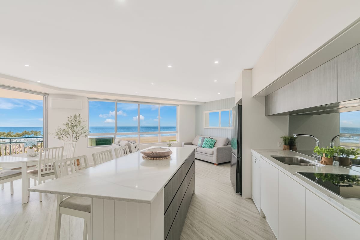 A modern kitchen with a large island, white cabinetry, and a view of the ocean.