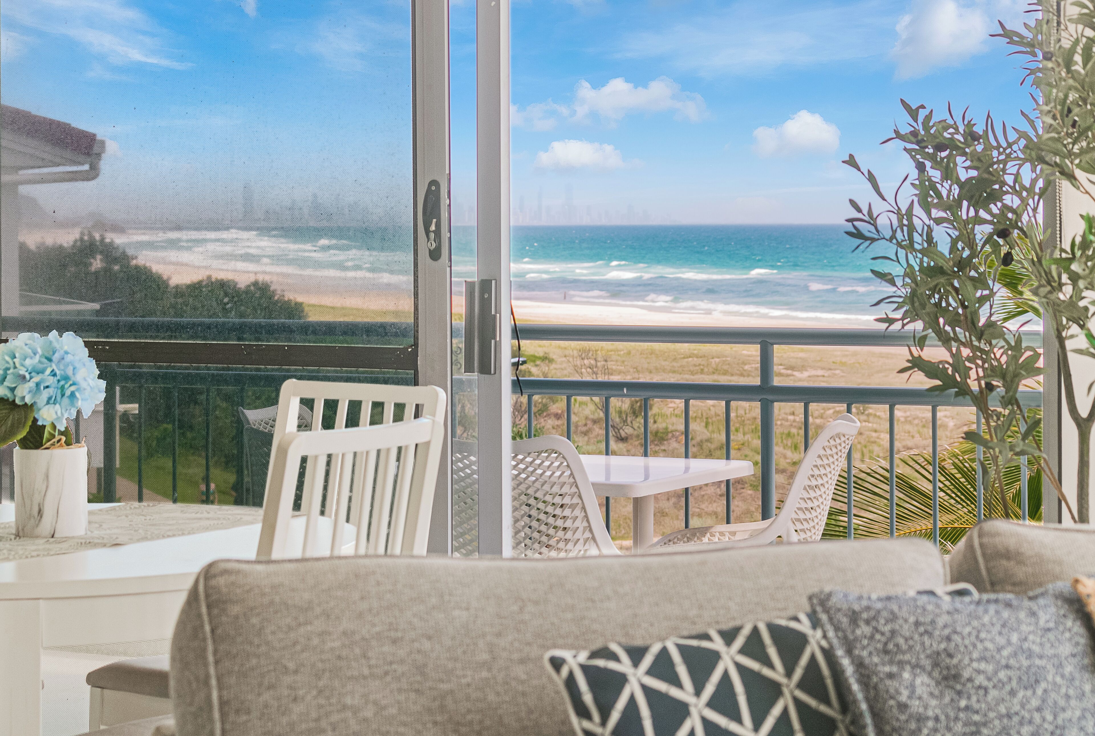 Un balcon donnant sur la plage, une chaise blanche, une petite table et une plante en pot.