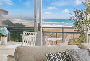 A balcony with a view of the beach, a white chair, a small table, and a potted plant. - Oceanside Resort (Bilinga)