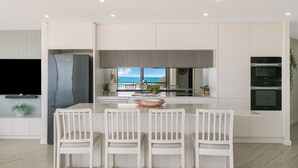 A modern kitchen with a large island, white cabinetry, and a view of the ocean. - Oceanside Resort (Bilinga)