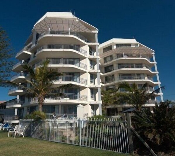 A multi-story hotel with balconies on each floor, surrounded by a fence and palm trees.