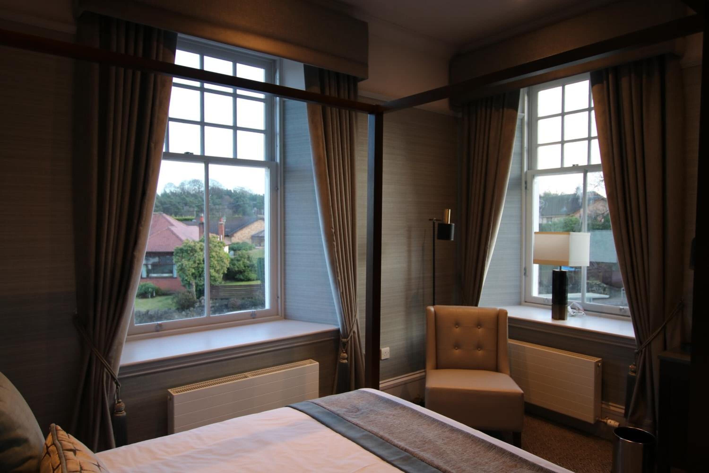 Une chambre d’hôtel avec un lit, une chaise, une lampe et des fenêtres avec des rideaux.