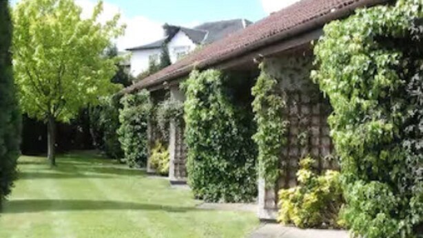 Uma fileira de edifícios de pedra com telhado de cerâmica, rodeada por vegetação cuidada e árvores.