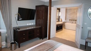 Quarto com cama, cómoda de madeira escura, televisão, banheiro com banheira e espelho.