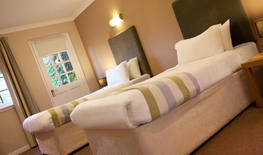 A double bed with a headboard, a bedside table, and a window with curtains.