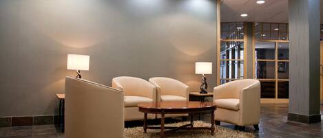 A lobby with three armchairs, a wooden coffee table, and two floor lamps.