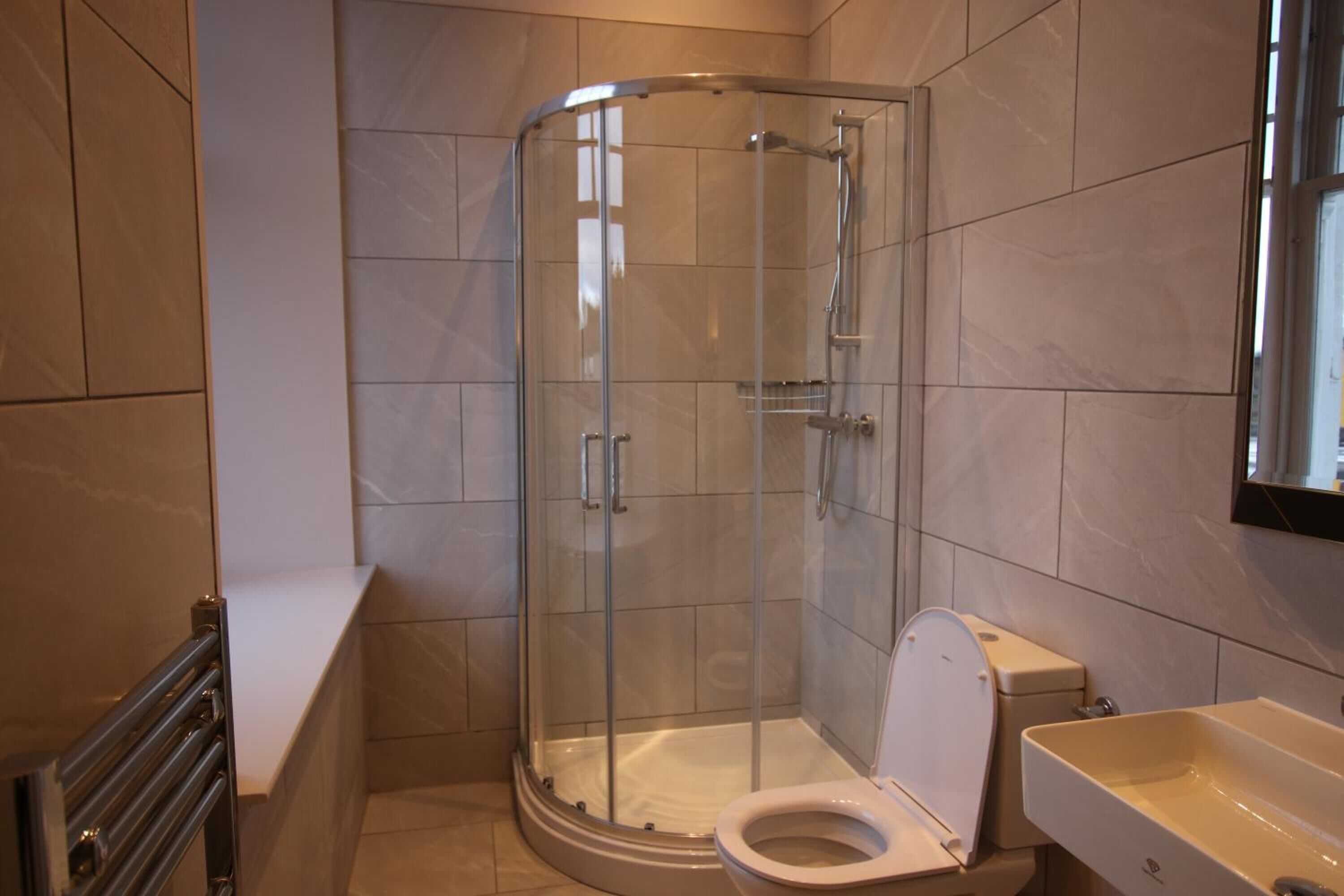 Et moderne badeværelse med et glasvæg-afskærmet brusebad, et hvidt toilet og en beige vask.