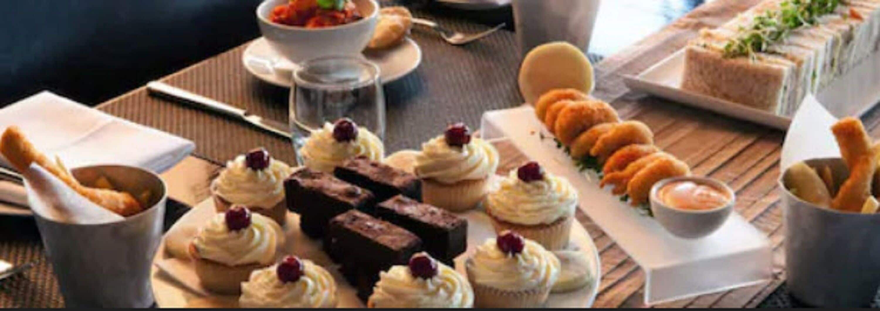 A table set with various desserts including cupcakes, brownies, and pastries, along with a bowl of soup and a glass of water.