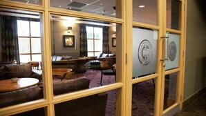 Quarto de hotel com área de estar, uma janela grande e uma porta com logotipo.